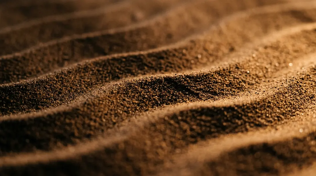 Macrofotografia di sabbia scura che forma onde parallele, ciascuna con un andamento leggermente diverso dalle altre.